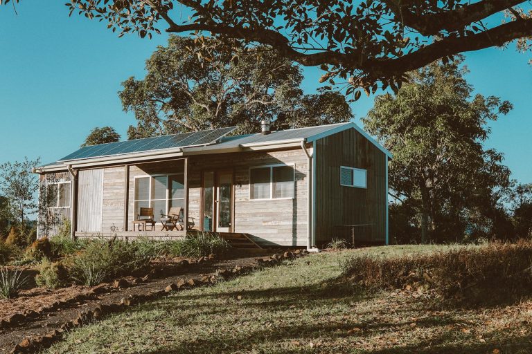 A charming wooden house in Australia featuring solar panels, surrounded by lush greenery.