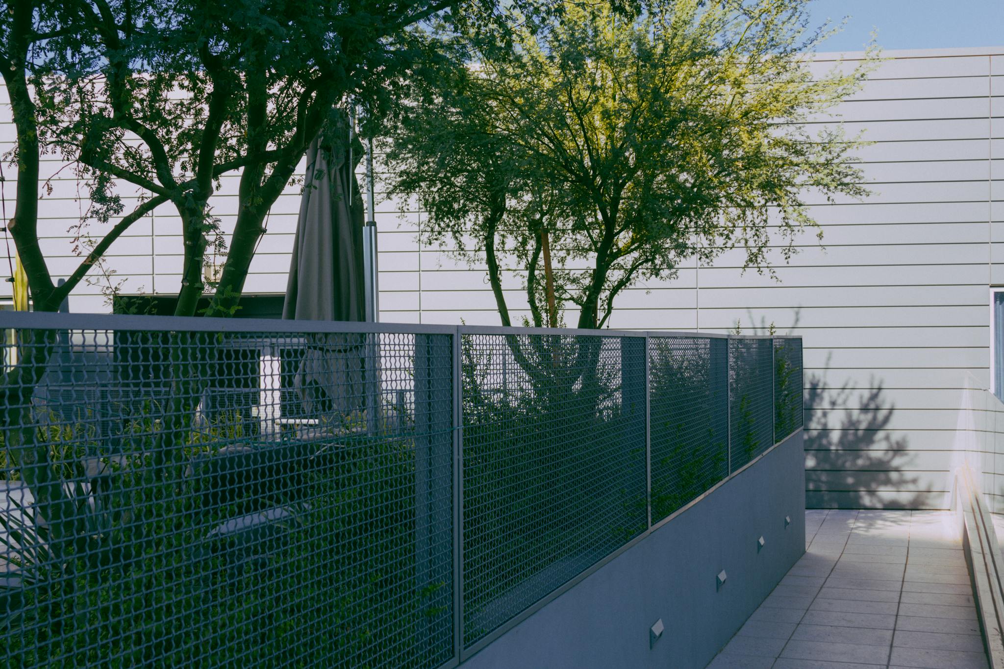 A contemporary urban patio with a metal fence, trees, and sunlight. Ideal for outdoor relaxation.