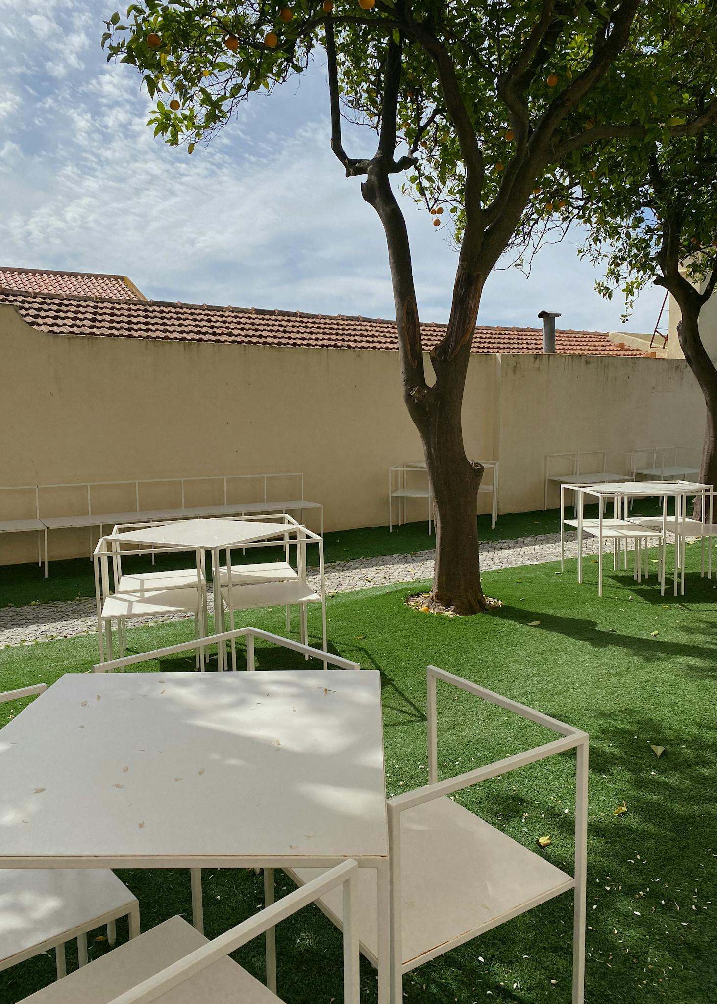 Modern white patio furniture under trees on a sunny day with a wall backdrop.