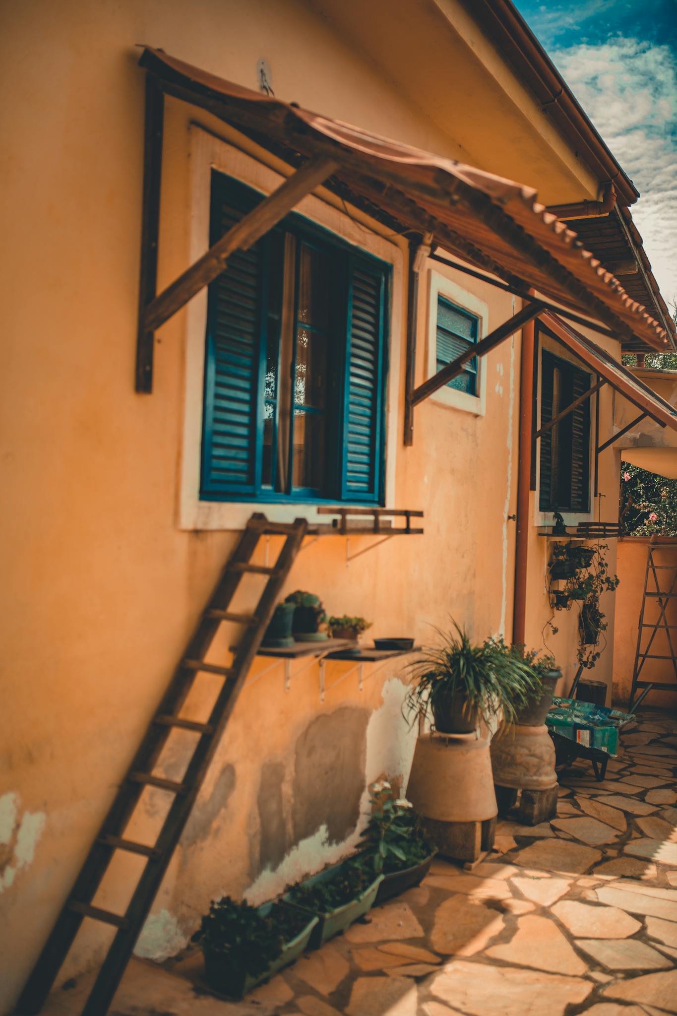 Quaint yellow house facade with blue shutter windows and garden pots.